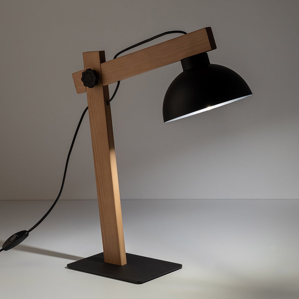 Lampa biurkowa z czarnym metalowym kloszem i drewnianą podstawą, z regulowanym ramieniem. Kabel z włącznikiem widoczny jest z boku lampy.