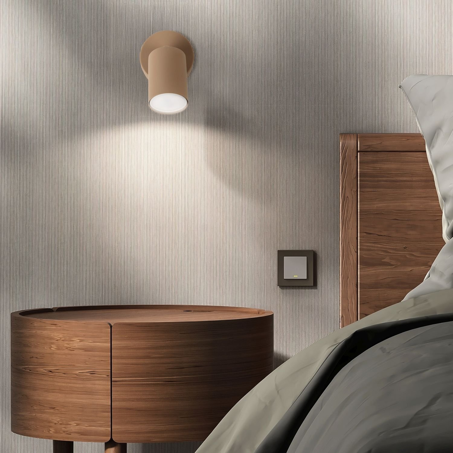 Na ścianie wisi beżowy reflektor sufitowy, który oświetla drewniany stolik nocny. Obok znajduje się drewniane łóżko z szarą pościelą oraz włącznik światła na ścianie.