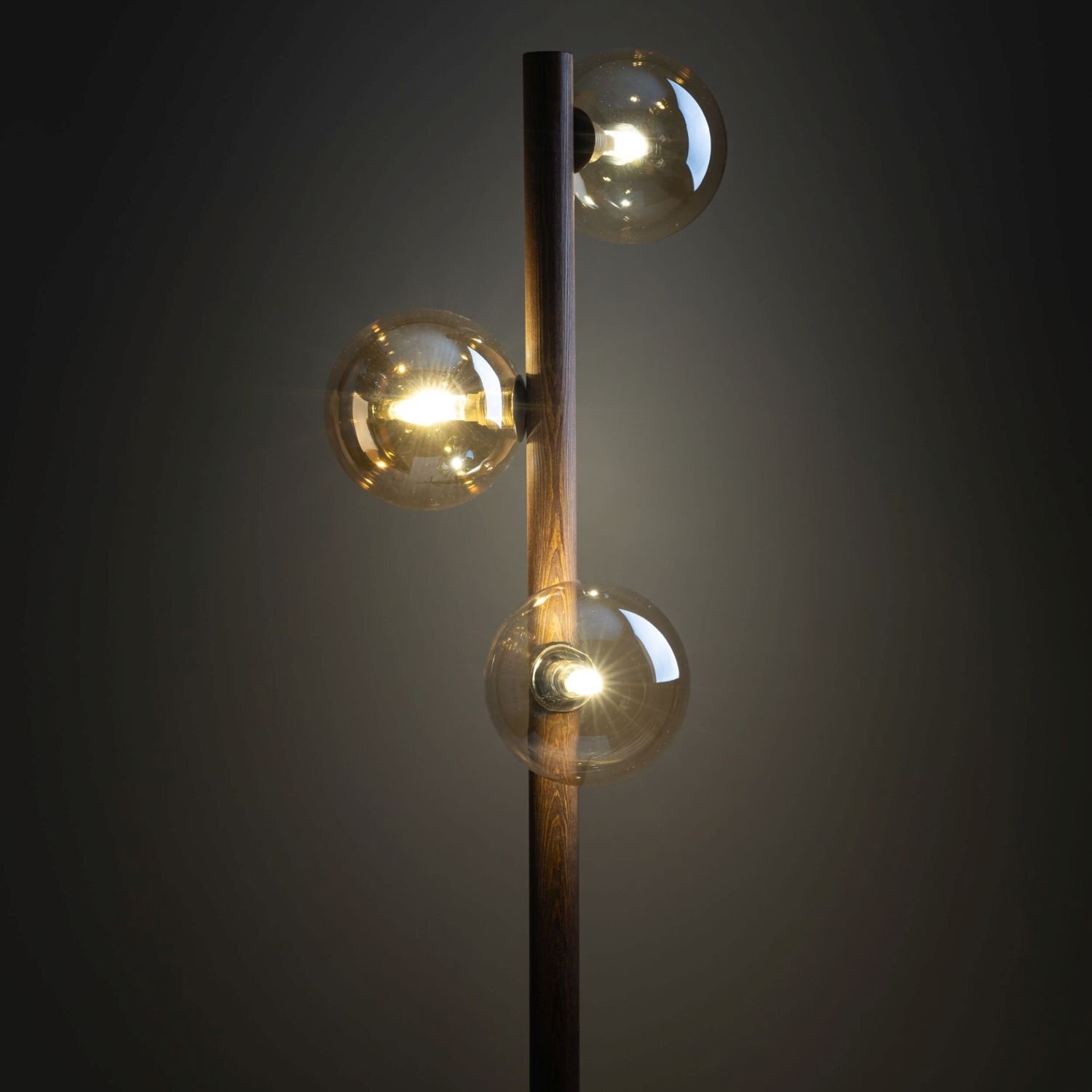 Lampa podłogowa z drewnianym stelażem i trzema szklanymi kloszami w kolorze bursztynowym. Klosze są kuliste i emitują ciepłe światło.