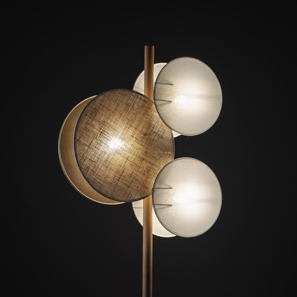 Lampa podłogowa z trzema okrągłymi kloszami w kolorze białym i jednym w kolorze brązowym, zamontowana na pionowym drewnianym trzonie. Klosze emitują ciepłe światło, a całość utrzymana jest w nowoczesnym stylu.