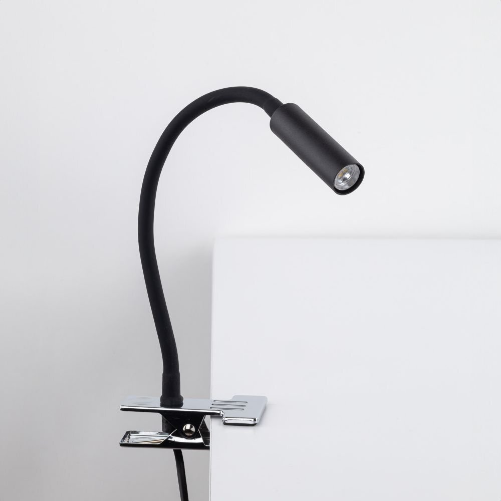 Czarna lampa biurkowa z klipsem przymocowana do białej powierzchni. Lampa ma elastyczne ramię i metalowy klosz.