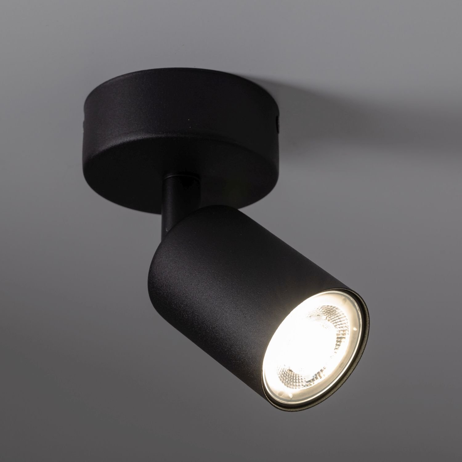 Czarny reflektor sufitowy z okrągłą podstawą i ruchomą głowicą, emitujący jasne światło. Produkt ma nowoczesny design i jest zamontowany na suficie.