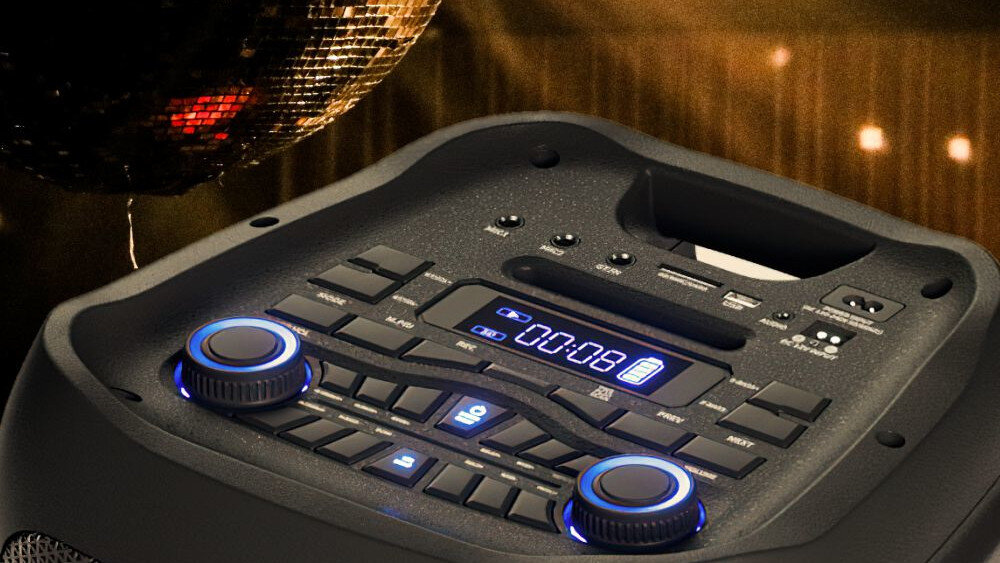 Zdjęcie przedstawia panel sterowania głośnika z wyświetlaczem pokazującym \'00:08\' oraz różnymi przyciskami i pokrętłami. W tle widoczna jest kula dyskotekowa.