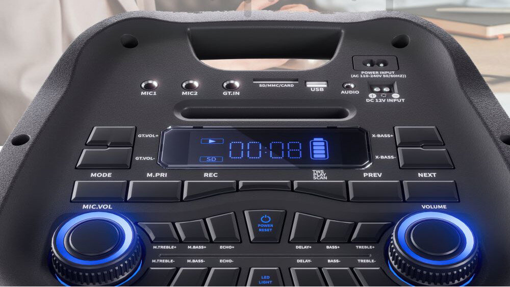 Panel sterowania głośnika z wyświetlaczem pokazującym \'00:08\' oraz ikoną baterii. Widoczne są przyciski do regulacji dźwięku, wejścia mikrofonowe i gitarowe, a także pokrętła z niebieskim podświetleniem.