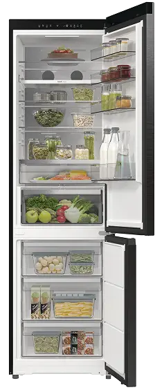 Otwarta lodówka z widocznymi półkami wypełnionymi różnorodnymi produktami spożywczymi, takimi jak warzywa, owoce, napoje i słoiki. W dolnej części znajdują się przezroczyste szuflady z dodatkowymi produktami.