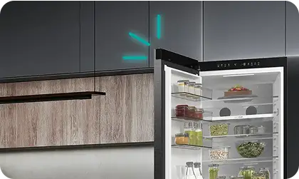 Otwarta lodówka z widocznymi półkami, na których znajdują się różne produkty spożywcze. W tle widać fragment kuchennej zabudowy z drewnianymi frontami.