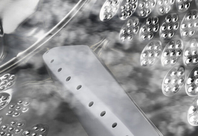 Wnętrze bębna pralki z widocznymi otworami i metaliczną powierzchnią. Obraz przedstawia szczegóły konstrukcji bębna z elementami odbijającymi światło.