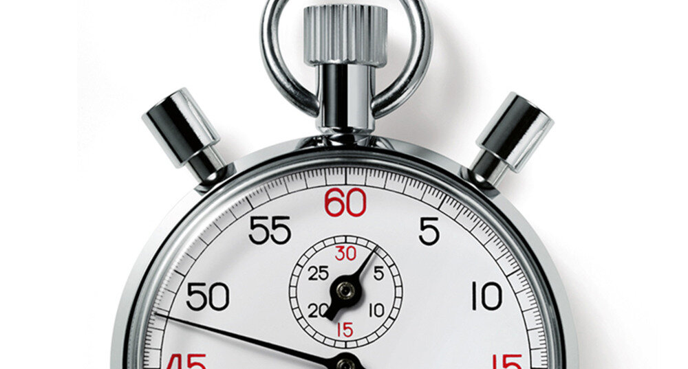 Zbliżenie na klasyczny stoper z białą tarczą, czarnymi i czerwonymi cyframi oraz srebrnymi przyciskami. Na tarczy widoczne są liczby od 5 do 60, a w środku mniejsza tarcza z liczbami od 5 do 30.