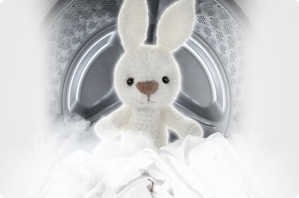 Pluszowy królik znajduje się wewnątrz bębna pralki, otoczony białymi tkaninami i parą.