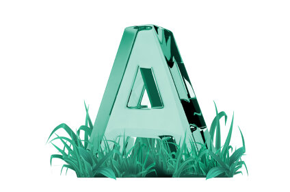 Szklana litera \'A\' w kolorze zielonym otoczona jest trawą.