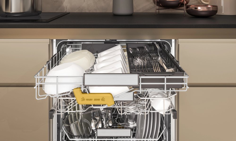 Otwarta zmywarka z widocznymi naczyniami i sztućcami w środku. Na górnym koszu znajdują się białe talerze i szklanki, a na dolnym koszu widoczne są talerze i sztućce.