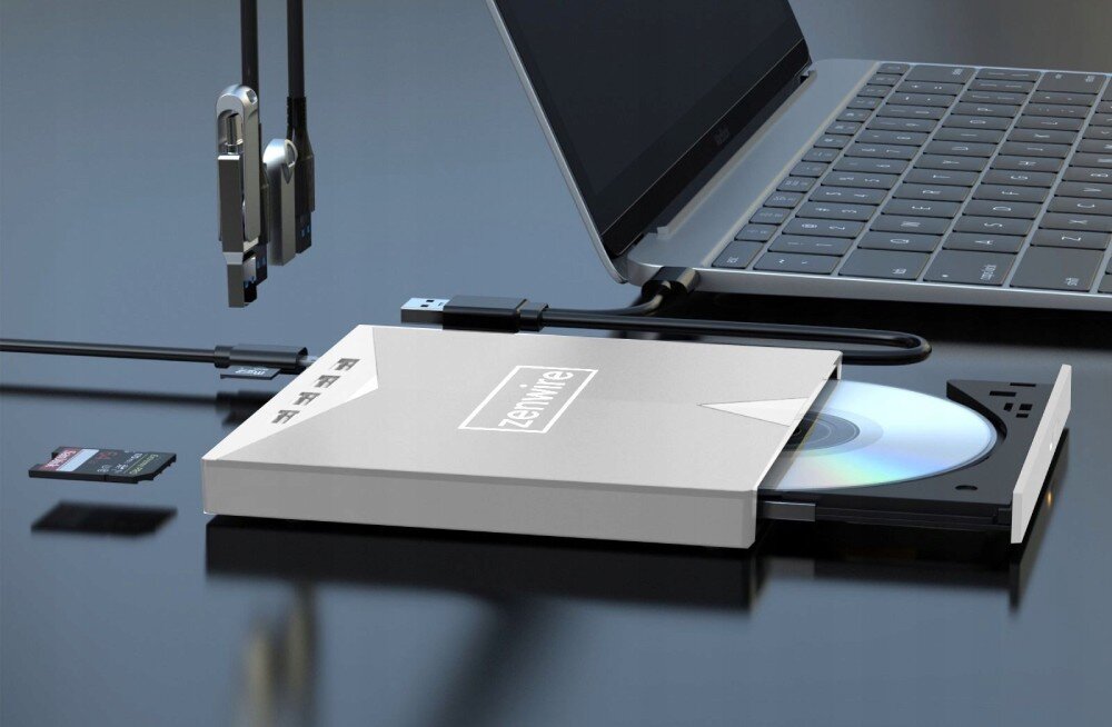 Na obrazie widoczny jest zewnętrzny napęd optyczny z logo \'zenwire\', podłączony do laptopa. Obok napędu leży karta pamięci i kilka kabli USB.