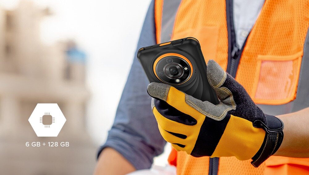 Osoba w pomarańczowej kamizelce trzyma smartfon z widocznym aparatem fotograficznym. Obok znajduje się ikona z napisem \'6 GB + 128 GB\'.