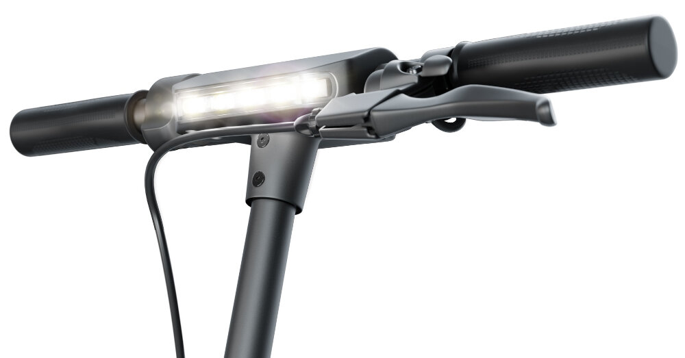 Zbliżenie na kierownicę czarnej hulajnogi elektrycznej z widocznym przednim światłem LED. Na kierownicy znajduje się dźwignia hamulca oraz przewód elektryczny.