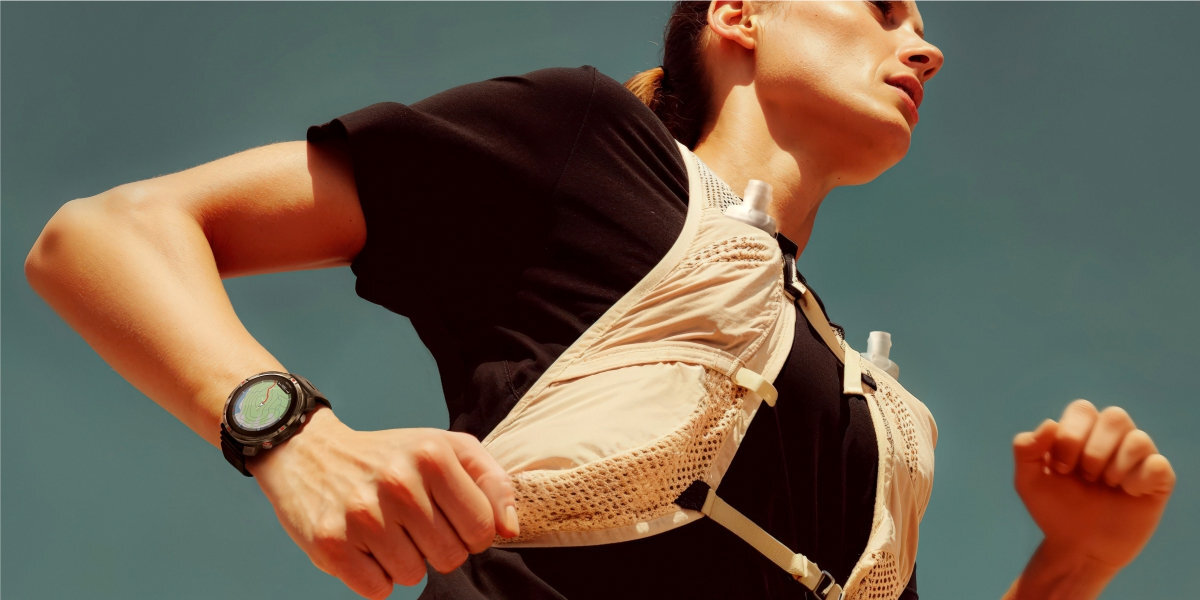 Osoba biegnąca w sportowym stroju, na nadgarstku widoczny czarny zegarek sportowy. Tło jest jednolite, niebieskie.