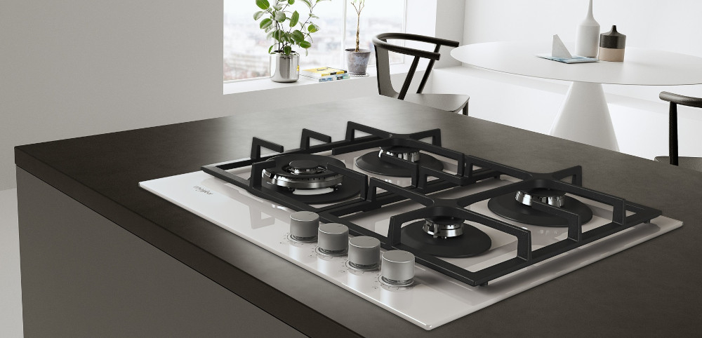 Na obrazie widoczna jest płyta gazowa z czterema palnikami i żeliwnymi rusztami, umieszczona na blacie kuchennym. W tle znajduje się stół z krzesłami oraz okno z widokiem na zewnątrz.