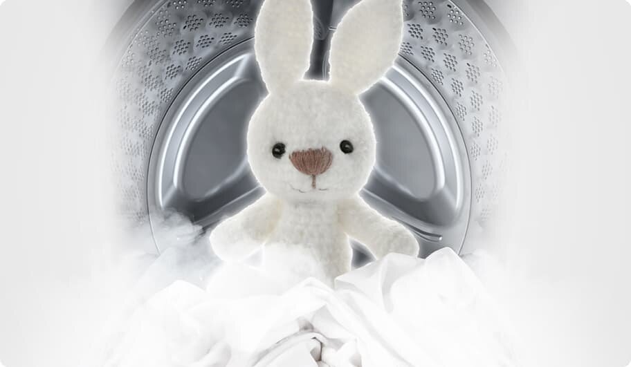 Wnętrze bębna pralki z widocznym pluszowym królikiem na tle białych tkanin. Królik jest biały z brązowym nosem i czarnymi oczami.
