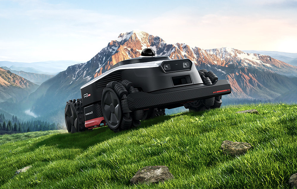 Czarny robot koszący z dużymi kołami znajduje się na zielonej trawie, w tle widać ośnieżone góry. Na robocie widoczny jest napis \'DREAME A3 AWD 1600\'.
