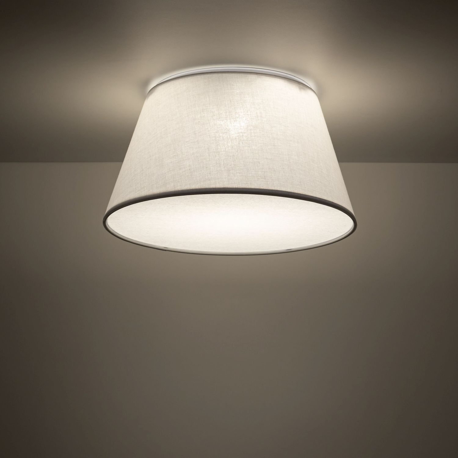 Na obrazie widoczna jest biała lampa sufitowa o cylindrycznym kształcie, zamontowana na suficie. Lampa emituje miękkie, rozproszone światło.