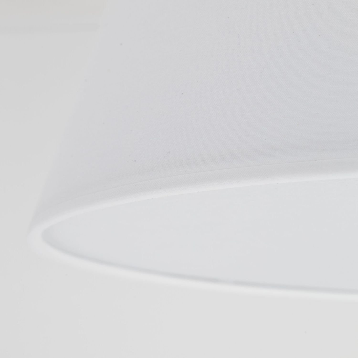 Zbliżenie na biały klosz lampy sufitowej o gładkiej powierzchni. Klosz ma prosty, nowoczesny design.