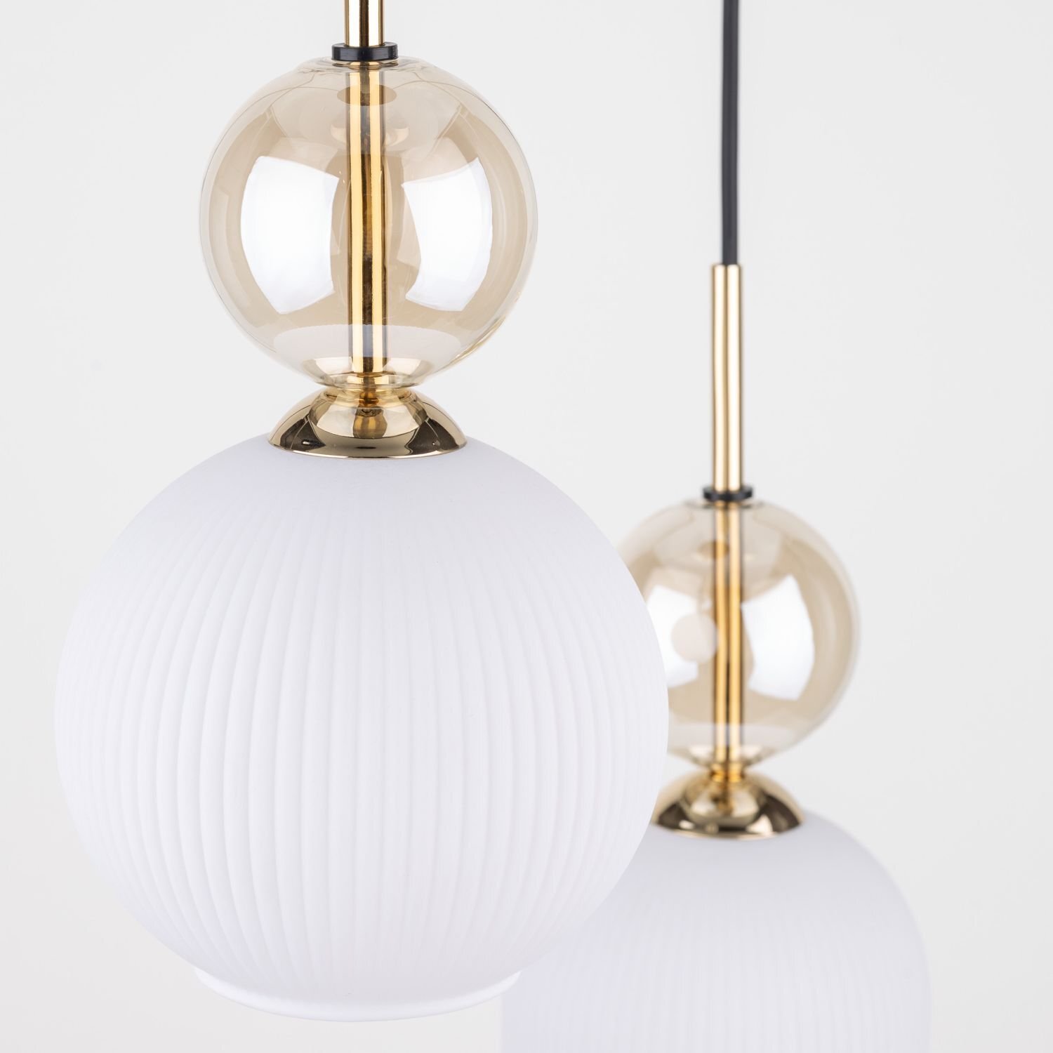 Zdjęcie przedstawia dwie wiszące lampy sufitowe z białymi, żebrowanymi kloszami i złotymi elementami dekoracyjnymi. Lampy mają elegancki, nowoczesny design.