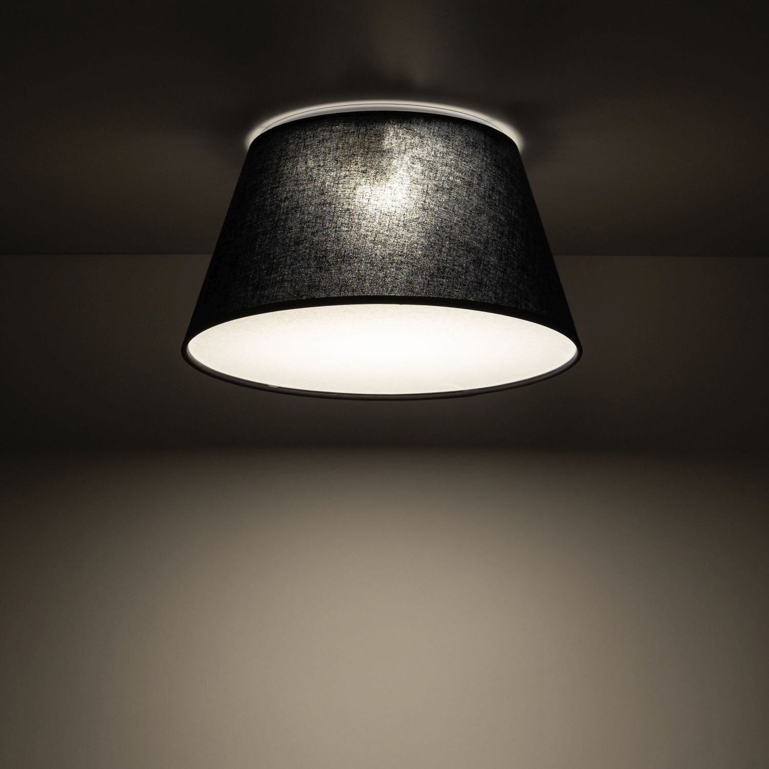Czarno-biała lampa sufitowa o stożkowym kształcie, emitująca ciepłe światło. Lampa jest zamontowana na suficie w ciemnym pomieszczeniu.
