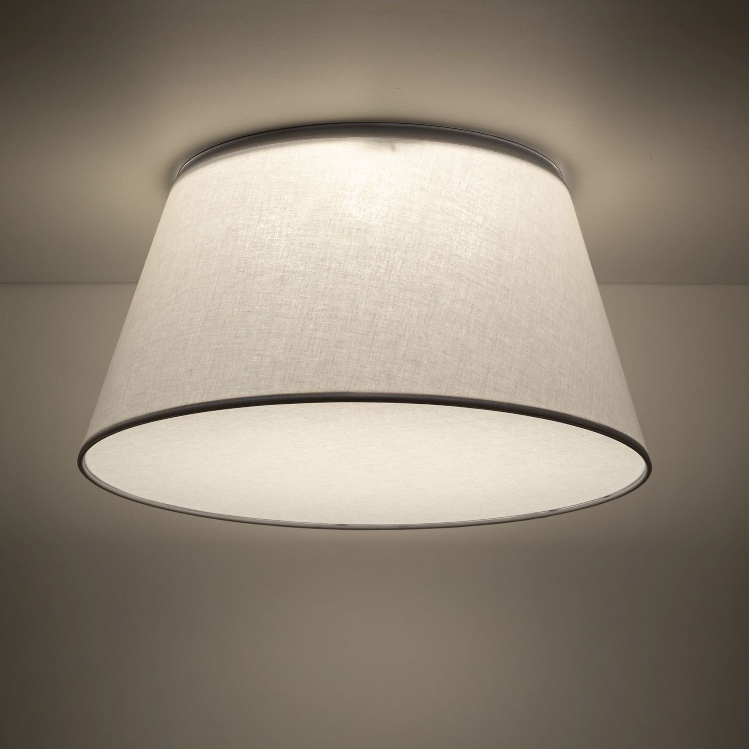 Na obrazie widoczna jest nowoczesna lampa sufitowa o białym, stożkowym kloszu. Lampa emituje miękkie, rozproszone światło.