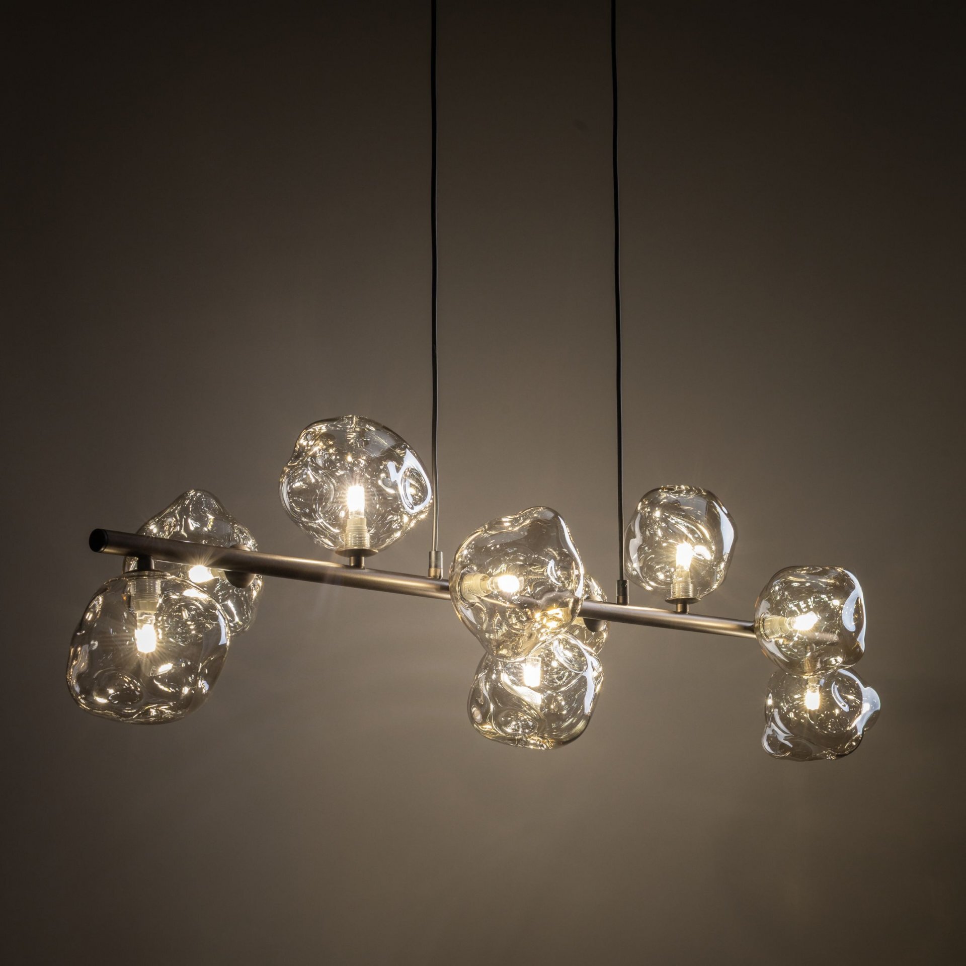 Lampa wisząca z dziewięcioma żarówkami umieszczonymi w bursztynowych, szklanych kloszach o nieregularnym kształcie. Konstrukcja lampy jest metalowa, a całość zawieszona jest na dwóch czarnych przewodach.