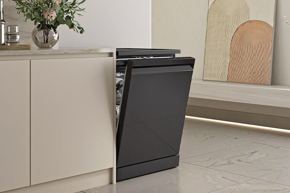 Zmywarka Samsung DW80H73YBFFU1 dostępna w Media Expert Zmywarka w kolorze czarnym jest częściowo otwarta, wkomponowana w nowoczesną kuchnię z jasnymi szafkami. Obok zmywarki stoi wazon z kwiatami, a na ścianie widać abstrakcyjne obrazy.
