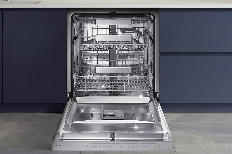 Otwarta zmywarka z widocznymi trzema poziomami koszy na naczynia, wykonana ze stali nierdzewnej. Na dolnej krawędzi widoczne jest logo \'SAMSUNG\'.