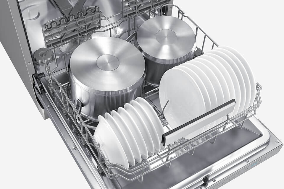 Wnętrze zmywarki z widocznymi metalowymi garnkami i białymi talerzami ułożonymi w koszu. Zmywarka jest otwarta, a naczynia są starannie rozmieszczone.