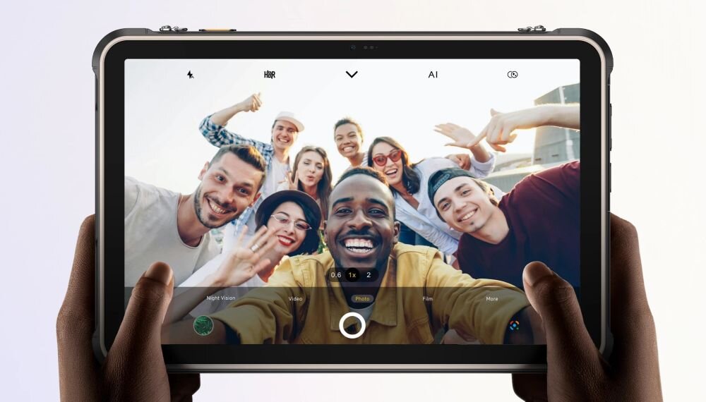 Tablet trzymany w dłoniach wyświetla zdjęcie grupy uśmiechniętych osób. Na ekranie widoczne są ikony aplikacji aparatu oraz przyciski sterujące.