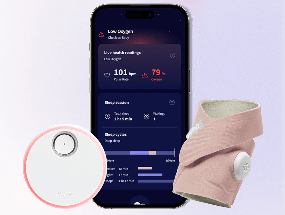 Na obrazie widoczny jest smartfon z aplikacją monitorującą zdrowie, pokazującą dane takie jak \'Pulse Rate 101 bpm\' i \'Oxygen 79%\'. Obok znajduje się różowy monitor oddechu w formie skarpetki oraz okrągłe urządzenie z logo \'Owlet\'.
