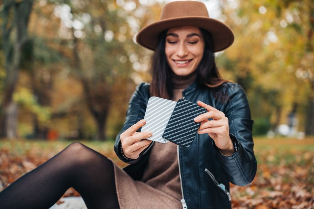 Dysk VERBATIM Store n Go 1TB HDD Srebrny Kobieta w kapeluszu i czarnej kurtce siedzi na tle jesiennych drzew i trzyma w dłoniach dwa dyski przenośne, srebrny i czarny