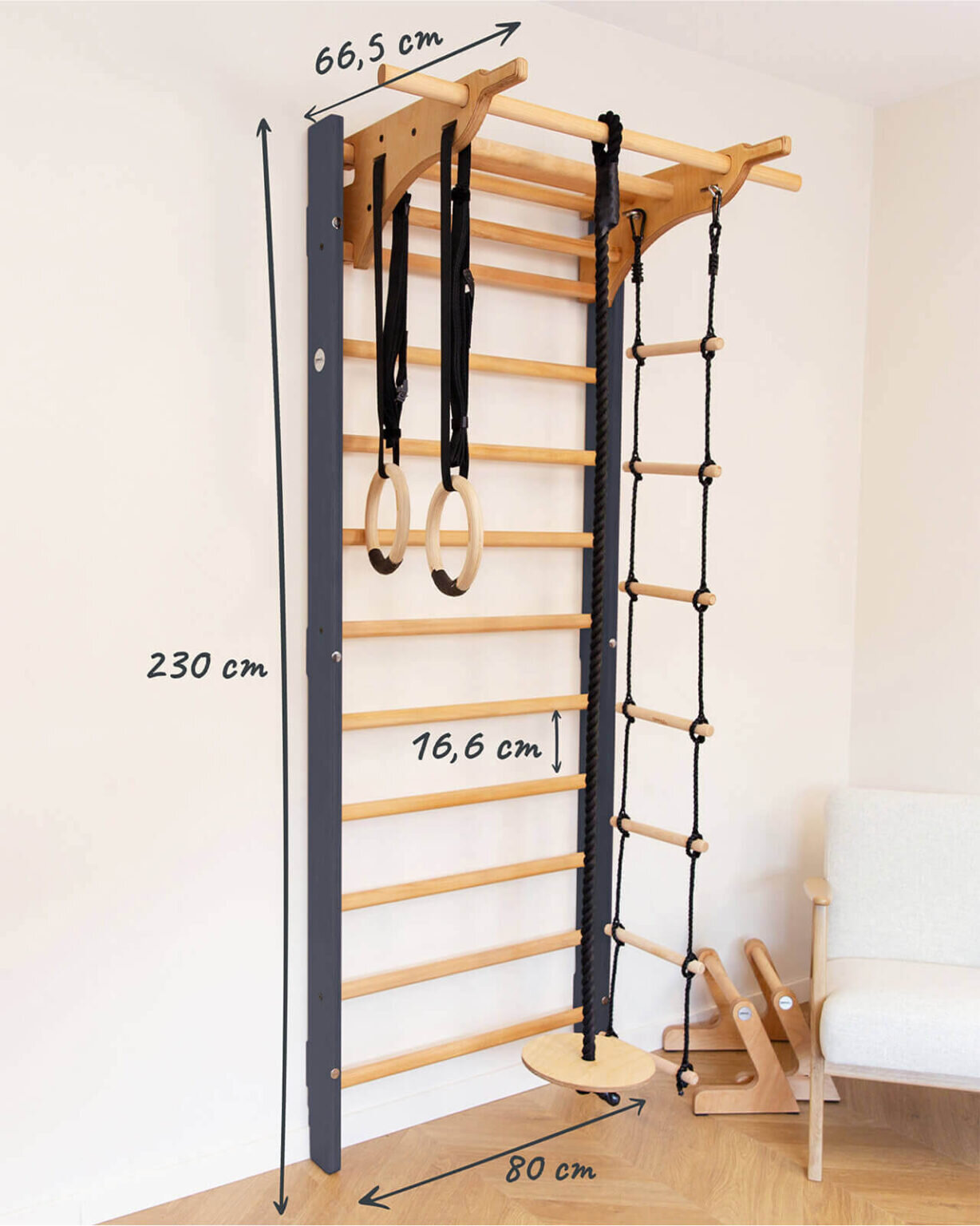 Drabinka gimnastyczna zamontowana na ścianie, wykonana z drewna i metalu, z dodatkowymi akcesoriami jak kółka gimnastyczne i lina z drabinką. Wymiary to 230 cm wysokości, 66,5 cm szerokości i 80 cm głębokości.