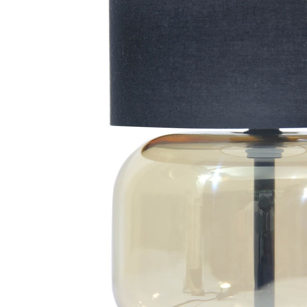 Obraz przedstawia fragment lampy stołowej z ciemnym abażurem i przezroczystą, bursztynową podstawą. Lampa ma nowoczesny design.