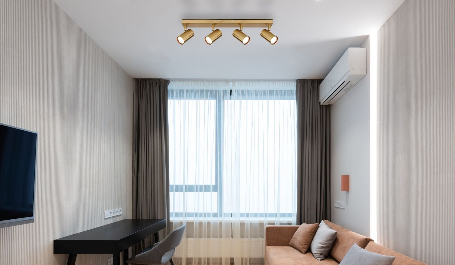 W nowoczesnym wnętrzu znajduje się lampa sufitowa z czterema regulowanymi reflektorami. Pomieszczenie jest jasne, z dużym oknem zasłoniętym przezroczystymi zasłonami, a na ścianie wisi telewizor.