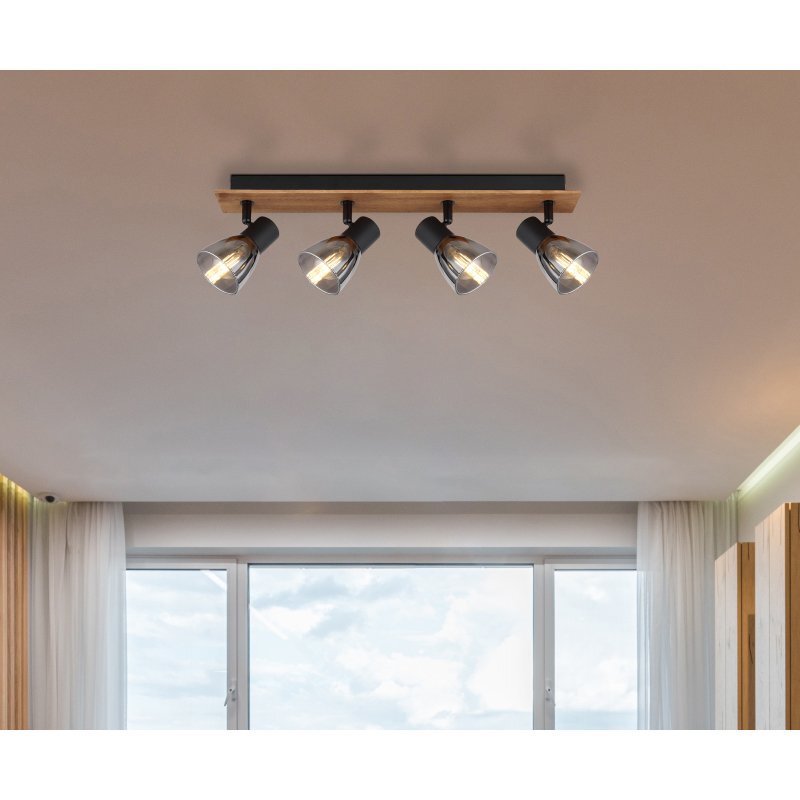 Na suficie zamontowana jest lampa sufitowa z czterema reflektorami, wykonana z drewna w kolorze brązowym i czarnego matowego metalu, z przydymionymi szklanymi kloszami. W tle widoczne jest okno z zasłonami i widokiem na niebo.
