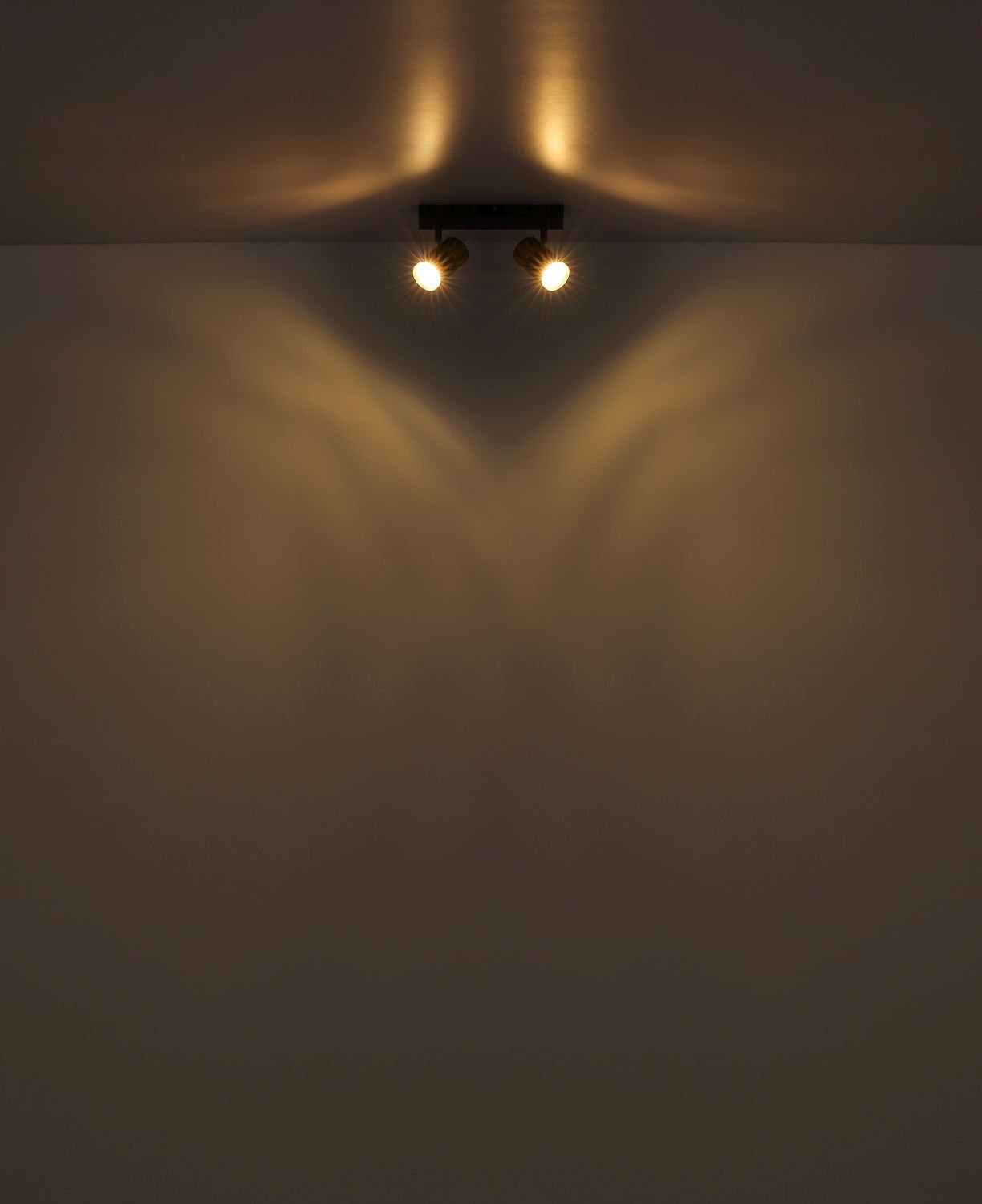 Na suficie zamontowana jest lampa sufitowa z dwoma źródłami światła, które emitują ciepłe, rozproszone światło na ścianę i sufit.