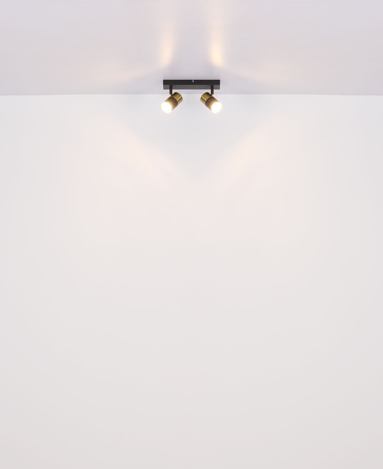 Na suficie zamontowana jest lampa sufitowa z dwoma regulowanymi reflektorami, które emitują światło na ścianę. Lampa ma nowoczesny design i jest w kolorze czarnym z elementami złotymi.