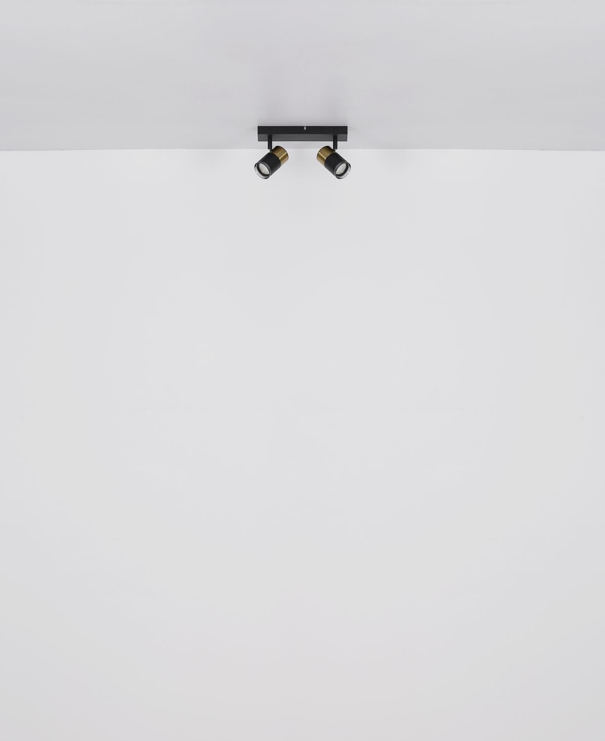 Na białym suficie zamontowana jest czarna lampa sufitowa z dwoma regulowanymi reflektorami. Reflektory mają złote akcenty wokół opraw.