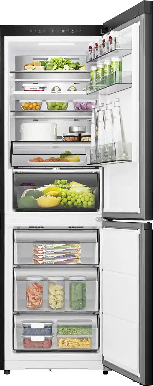 Otwarta lodówka z widocznymi półkami wypełnionymi różnorodnymi produktami spożywczymi, takimi jak warzywa, owoce, napoje i pojemniki z jedzeniem. Na drzwiach znajdują się butelki i kartony, a w dolnej części lodówki widoczne są zamrażalnikowe szuflady z mrożonkami.