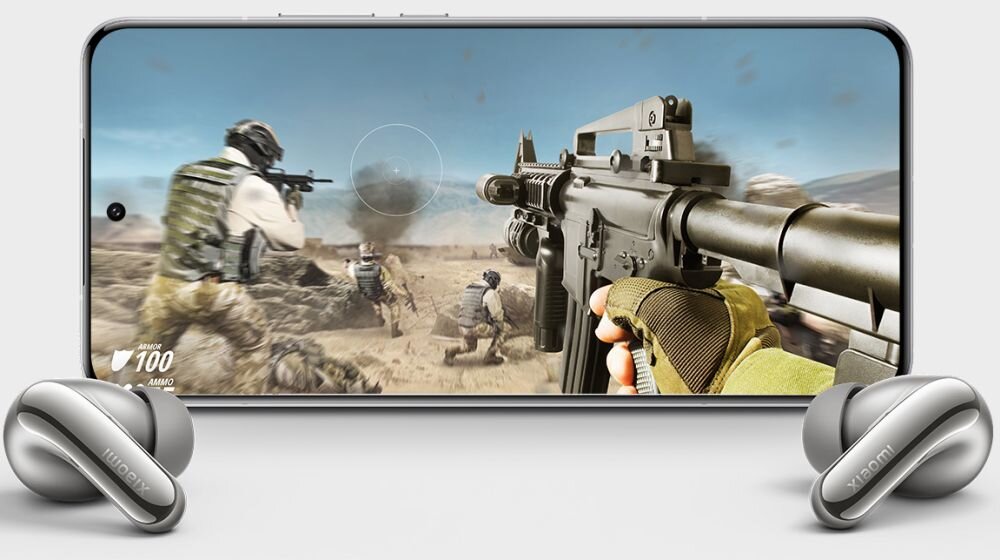 Na obrazie widoczny jest smartfon z wyświetlonym na ekranie dynamicznym ujęciem z gry akcji, przedstawiającym żołnierzy i broń. Przed telefonem znajdują się słuchawki dokanałowe w kolorze tytanowym z widocznym logo \'xiaomi\'.