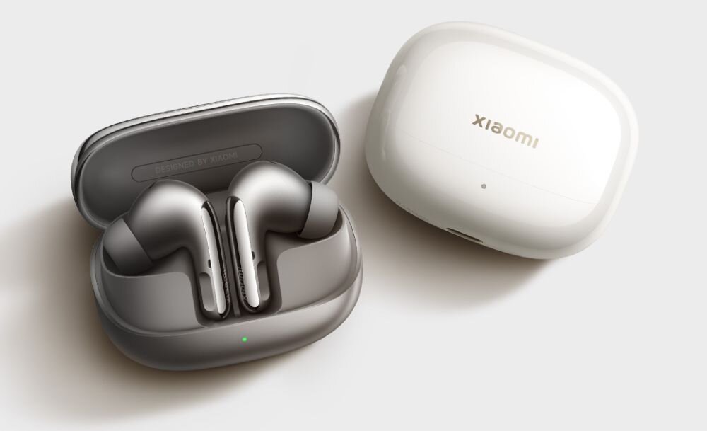 Na obrazie widoczne są słuchawki dokanałowe w otwartym etui oraz zamknięte etui z napisem \'xiaomi\'. Słuchawki mają metaliczny kolor, a etui jest białe.