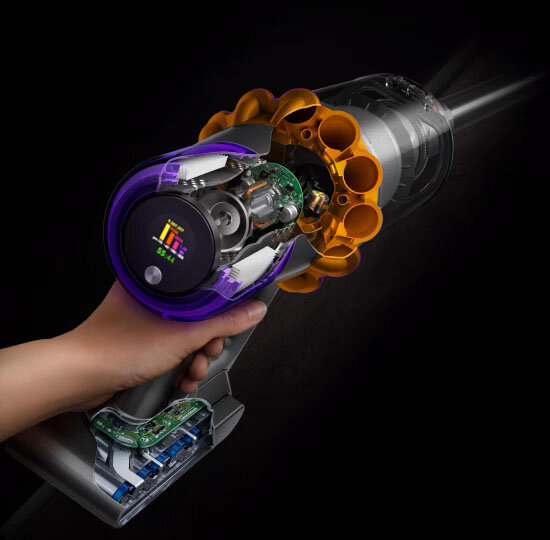 Osoba trzyma odkurzacz z widocznym wnętrzem, ukazującym mechanizmy i elektronikę. Odkurzacz ma fioletowe i pomarańczowe elementy oraz wyświetlacz z kolorowymi paskami.
