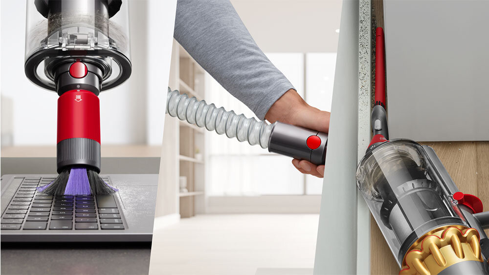 Obraz przedstawia odkurzacz z czerwonym i szarym elementem, używany do czyszczenia klawiatury oraz wąskiej przestrzeni przy ścianie. Widać przezroczysty pojemnik na kurz i elastyczną rurę ssącą.