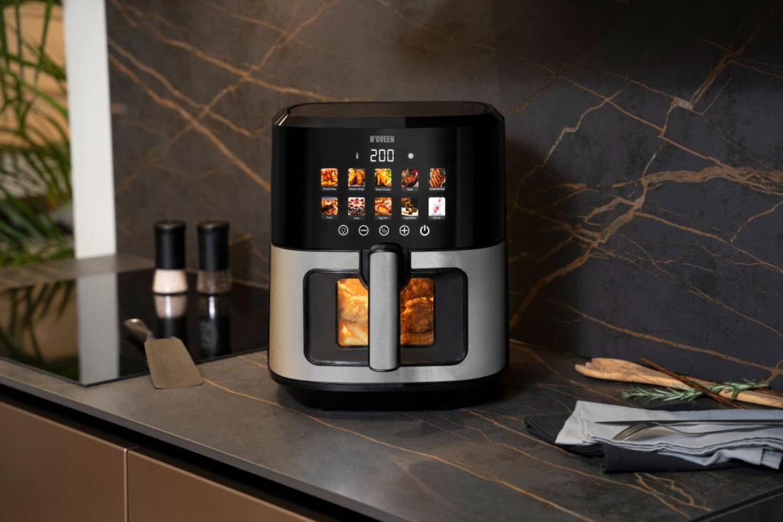 Na blacie kuchennym stoi frytkownica beztłuszczowa z wyświetlaczem pokazującym temperaturę 200 stopni oraz różne ikony potraw. Obok znajdują się solniczka i pieprzniczka, łopatka oraz złożone serwetki.