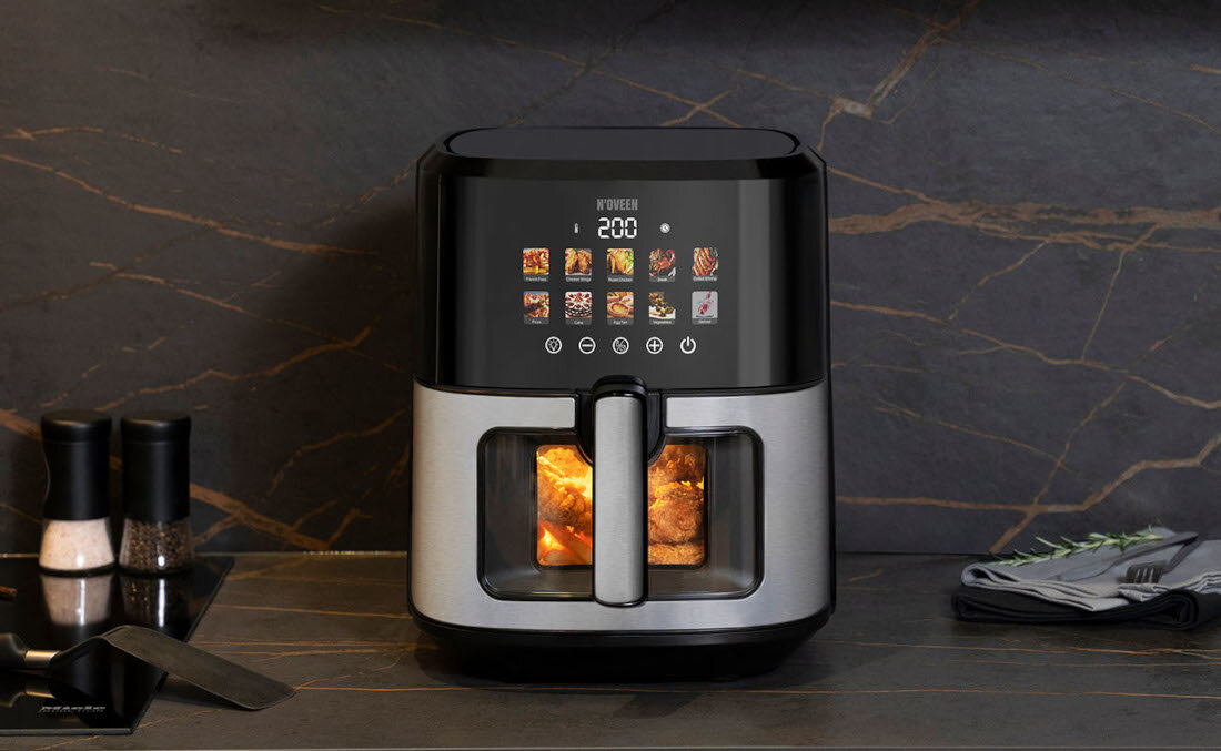 Na blacie kuchennym stoi frytkownica beztłuszczowa z wyświetlaczem pokazującym temperaturę 200 stopni i różne ikony potraw. Obok znajdują się solniczka, pieprzniczka, łopatka i złożone serwetki.