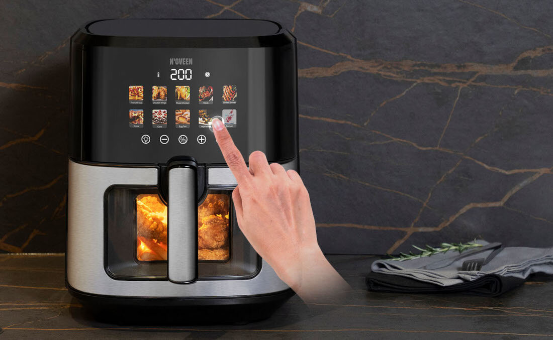 Frytkownica beztłuszczowa z wyświetlaczem dotykowym, na którym widoczne są różne ikony potraw oraz liczba \'200\'. Na blacie obok urządzenia leżą złożone szare serwetki i sztućce.