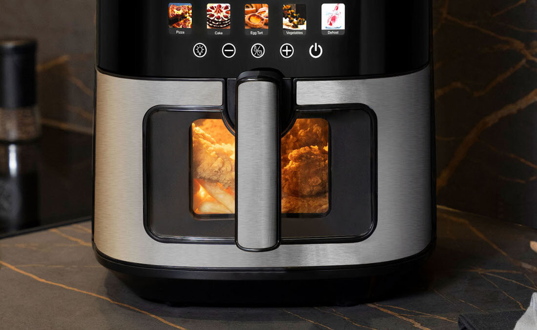 Frytkownica beztłuszczowa z metaliczną obudową i przezroczystym okienkiem, przez które widać piekące się jedzenie. Na górze panel z ikonami różnych trybów gotowania.